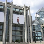 La façade du MBAC sur laquelle on voit un accrochage d'une série de photos sur fond blanc représentant un femme et un homme.
