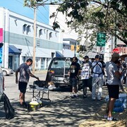 Un homme se tient debout près d'un barbecue et d'autres grèvistes attendent en fil pour se servir sur un trottoir par une journée ensoleillée à Vancouver. 