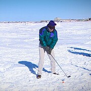 Un golfeur s'apprête à frapper une balle dans la neige, sur la banquise, en face du centre-ville de Rimouski.