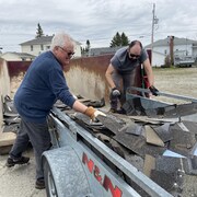 Deux hommes transfèrent de vieux matériaux de construction d'une remorque à un gros bac à déchets.