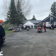 Plusieurs motocyclettes se trouvent devant une maison. Quelques hommes avec des vestes en cuir sont présents.