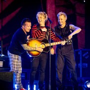 Les trois membres du groupe sourient sur scène. 
