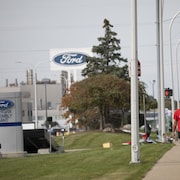 Un gréviste qui fait du piquetage sur le trottoir devant une usine de Ford tient une pancarte qui porte la mention « UAW en grève » en anglais.