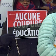 Des enseignants tiennent des pancartes, dont une avec le message « aucune coupure en éducation ».