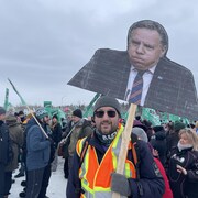 Un travaille tient une pancarte où on aperçoit le premier ministre François Legault en photo.