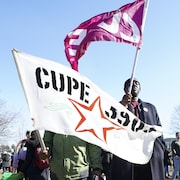 Deux personnes tenant des drapeaux du syndicat lors d'un rassemblement sur le terrain de l'Université.