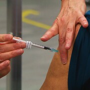 Deux mains de dame effectuent une piqûre avec une seringue sur le bras d'un patient.