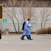 Un travailleur de la santé portant un équipement de protection individuelle accompagne un patient dans un centre d'évaluation de l'Autorité de la santé de la Saskatchewan.