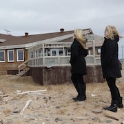 Deux femmes regardent l'arrière d'un bâtiment menacé par l'érosion.