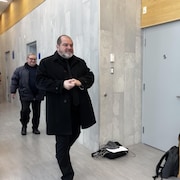 Un homme en manteau noir dans un palais de justice.