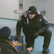 Un policier discute avec un itinérant assis dans un couloir de métro, à Montréal.