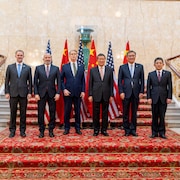 Des hommes posent debout devant des drapeaux chinois et am&eacute;ricains.