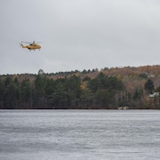 Un hélicoptère survole un plan d’eau dans un ciel gris.