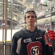 Un joueur de hockey des 67 avec son équipement pose pour une photo devant la patinoire.