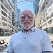 Un homme souriant prend la pose, devant une œuvre en forme d'anneau dans un centre-ville.