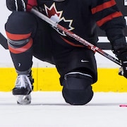 Un joueur de hockey en uniforme avec un genou posé sur la glace. On voit le logo de Hockey Canada sur son chandail.