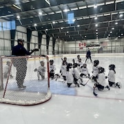 Sur glace, de jeunes joueurs de hockey entourent un filet de hockey ainsi que leur entraîneur.