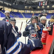 Des joueuses de hockey sur le bord d’une patinoire avec des gourdes déposées sur la bande près d’un banc.