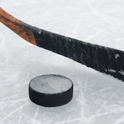 Un bâton de hockey et une rondelle sur la glace.