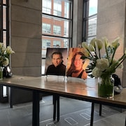 Les portraits de Daniel Langlois et de Dominique Marchand sont posés sur une table et entourés de deux bouquets de fleurs.