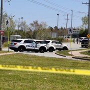 Quatre véhicules de police et un ruban jaune bloquent une rue.