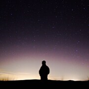 Une personne regarde l'horizon dans une nuit étoilée.