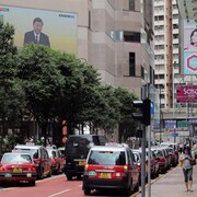 Des taxis immobilisés dans une rue à Hong Kong et un écran géant sur lequel est présenté un discours de Xi Jinping.