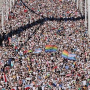 Les manifestants marchent sur un pont avec des drapeau de la fierté.