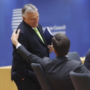 Viktor Orban rit en recevant une accolade de Mark Rutte dans une salle de conférence.