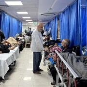 Des patients dans un corridor d'hôpital, certains sur des lits de fortune, d'autres debout. 