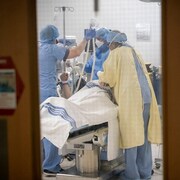 Du personnel médical entoure un individu sur une table d'opération.