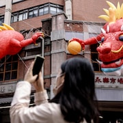 Une personne photographie un dragon gonflable accroché à un édifice.