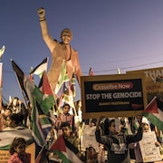 Des gens agitent des drapeaux et des pancartes sur lesquelles est écrit «Arrêtez le génocide».