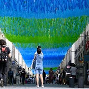 Une femme prend en photo une ombrière verte et bleue dans le centre-ville de Rennes.