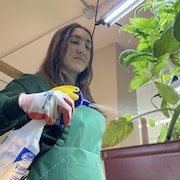 Karina Kirwan qui porte un tablier et des gants entrain d'arroser une plante.