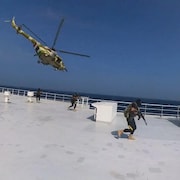 Un hélicoptère au-dessus d'un cargo où des rebelles marchent.