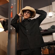 Hubert Lenoir porte un chapeau beige et une grande chemise noire dans un studio d'enregistrement. 