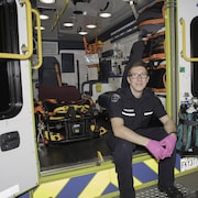 Un homme portant un uniforme d’ambulance assis sur la première marche derrière l’ambulance.