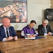 Trois personnes assises à une table signe un document.
