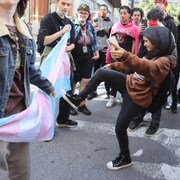 Une jeune femme donne un coup de pied dans un drapeau de la Fierté que transportent d'autres jeunes gens dans une manifestation.
