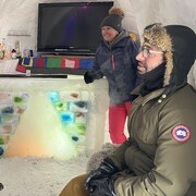 Trois adultes à l'intérieur d'un abri de neige sourient.