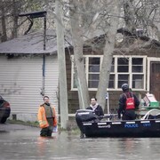 Des policiers, dans un bateau, parlent à des citoyens inondés.