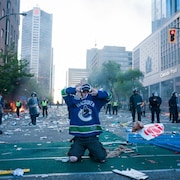 Un partisan de l'équipe des Canucks de Vancouver a genoux devant des policiers dans une rue jonchée de débris.