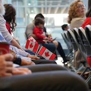 Des gens assis tiennent de petits drapeaux du Canada.