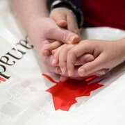 Des mains entrelacées sur un sac orné d'une feuille d'érable et du mot Canada.