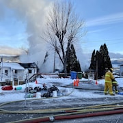 Des pompiers et des tuyaux devant une maison incendiée et entourée de fumée.
