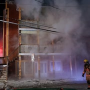Un pompier marche devant une maison en flammes.