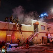 Des pompiers montent dans une échelle pour accéder à la toiture du bâtiment.