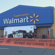 Un ruban délimite un périmètre de sécurité devant un magasin Wal-Mart. Une camionnette de la Sûreté du Québec est stationnée devant l'entrée. 