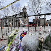 Des fleurs déposées près d'une barrière en métal devant un édifice incendié.